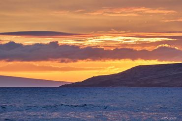 Sunset over ocean with silhouetted hills and vibrant clouds.