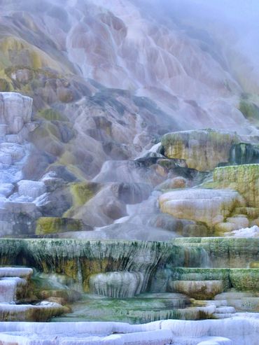 Steaming mineral terraces with pastel hues and misty atmosphere.