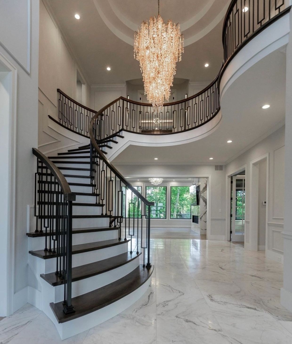 Elegant curved staircase with chandelier in modern home foyer.