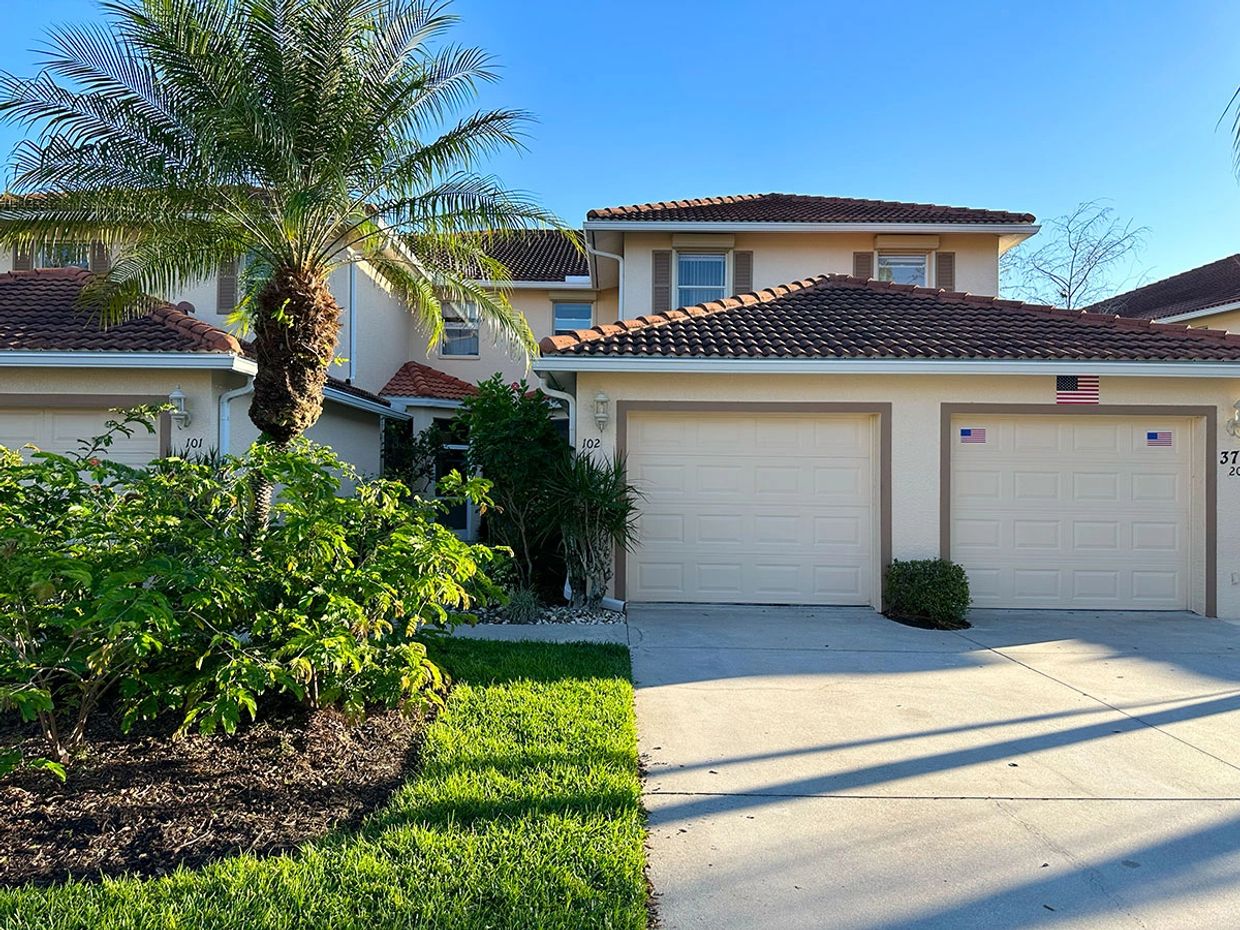 Suburban homes with garages and palm trees under a clear blue sky.