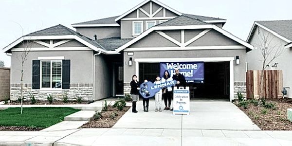 Family celebrating with a large key in front of a new home.