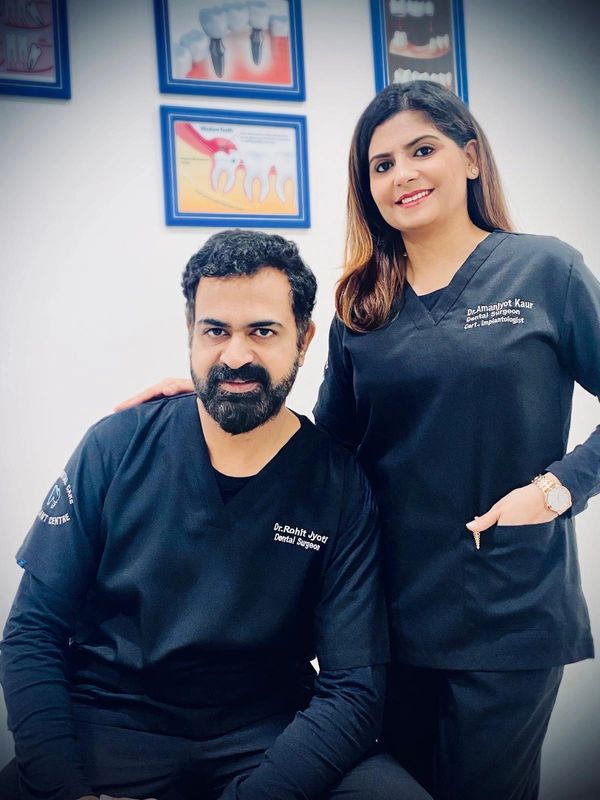 Two dental surgeons posing in a clinic with dental health posters behind them.