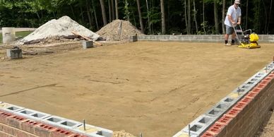 Man working on compacting soil inside a brick foundation at a construction site.