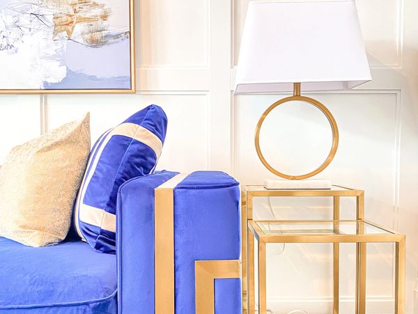 a closeup of a blue sofa with gold accents and nesting gold side tables with a gold circular lamp.