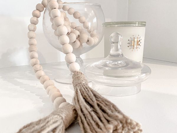 a glass jar with wooden bead garland coming out of it. right beside it is a white candle and the lid
