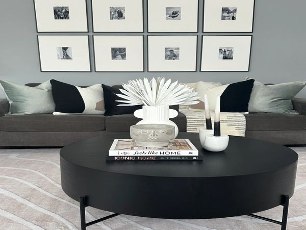 Modern living room with a dark round coffee table and gray sofa with decorative pillows.