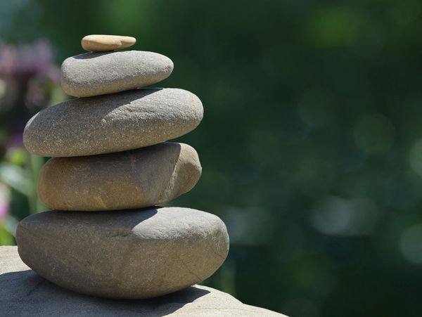 a closeup of a stack of rocks in big to small sizes resting on a surface with greenery in the back