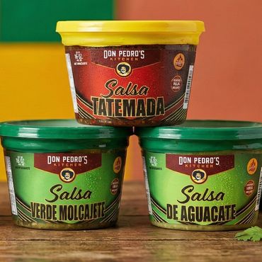 Various Don Pedro's Kitchen salsas in colorful containers on a wooden surface.