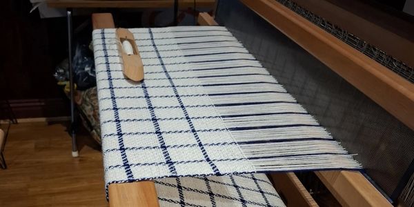 Wooden loom weaving a white and blue checkered fabric.