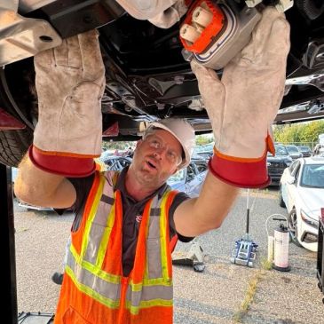 Worker in safety gear inspecting vehicle underside.
