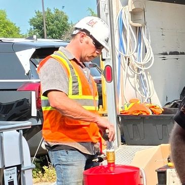 Worker in orange safety vest refilling a container.