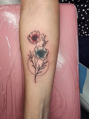 Delicate tattoo of two flowers with colored petals and dotted circle.