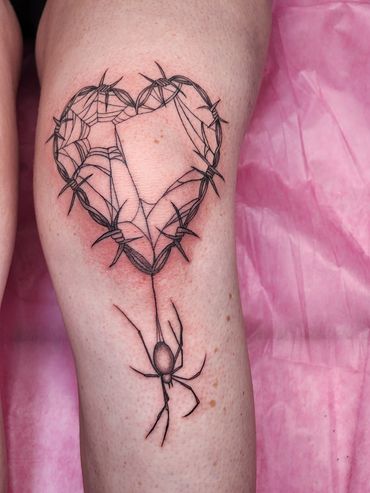 Tattoo of a spider weaving a heart-shaped web made of barbed wire.