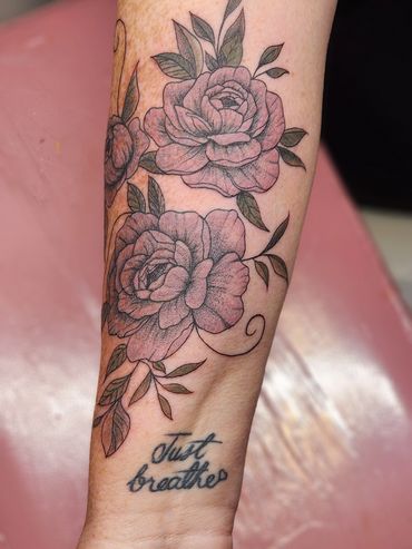 Floral tattoo with "Just breathe" script on wrist.