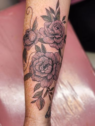 Forearm tattoo of roses and leaves in black ink.