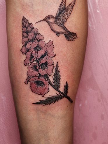 Delicate tattoo of a hummingbird and flowers on skin.