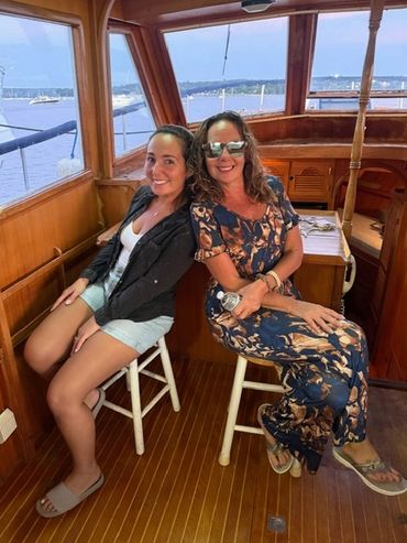 Two women sitting and smiling on a boat with a scenic water view.