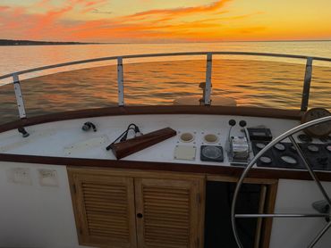 Boat steering wheel and controls at sunset over calm water.