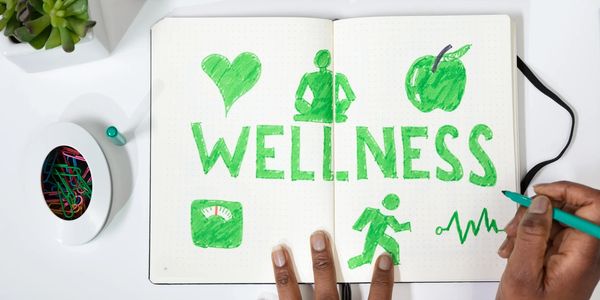 Person drawing wellness-related icons and text in a notebook on a desk.