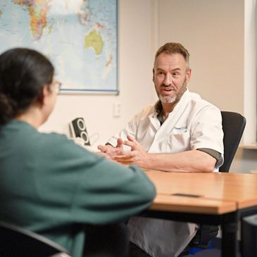 Doctor in a white coat consulting a patient in an office with a world map.