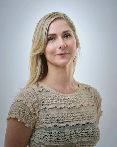 Smiling woman with blonde hair in lace beige top.