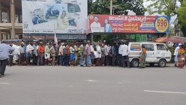 People lined up on a street near a white van with billboards in the background.