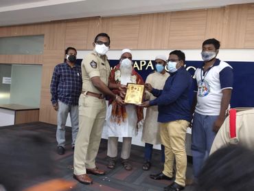 Group of men, including a police officer, exchanging a plaque indoors, all wearing masks.