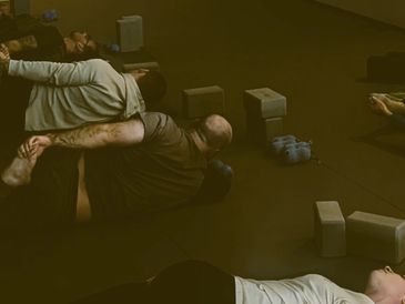 People practicing yoga with blocks in a dimly lit room.