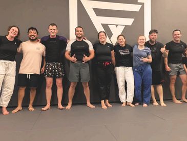 Group of nine people standing barefoot in martial arts attire.