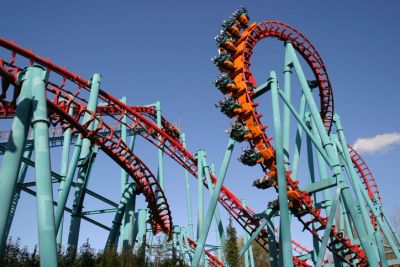 Thrill-seekers ride an orange roller coaster on a clear day.