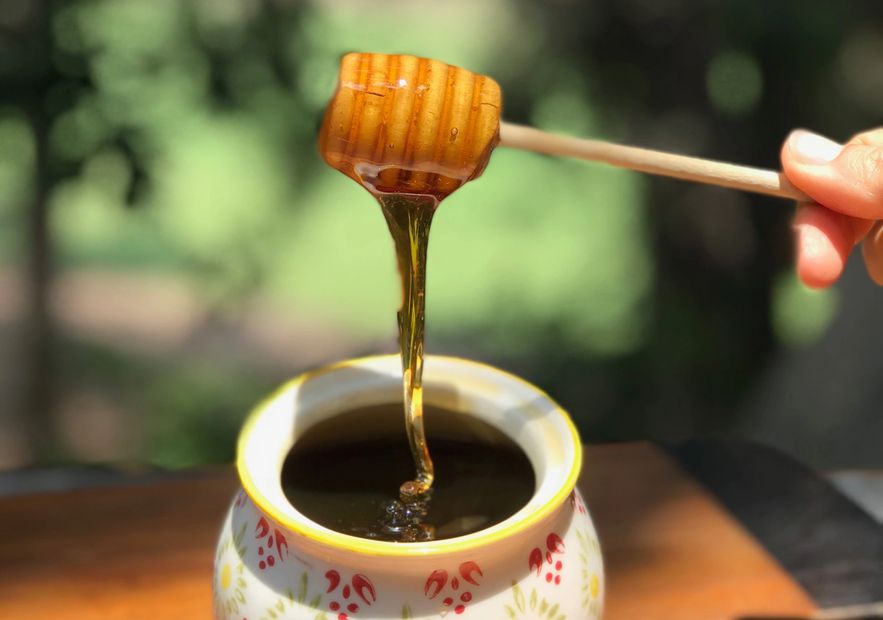Honey dripping from a wooden dipper into a floral jar.