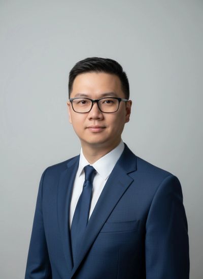 Professional man in navy suit and glasses posing against a gray background.