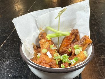 Bowl of saucy chicken wings garnished with green onions and celery sticks on a dark wooden table.
