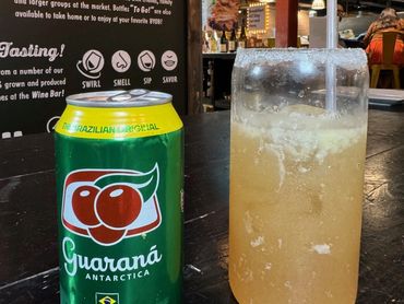 Can of Guaraná Antarctica soda next to a sugar-rimmed glass with a straw on a dark table.