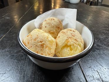 Three pieces of Brazilian cheese bread in a bowl on a rustic table.