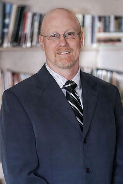 A middle-aged man in a suit and tie smiling in front of bookshelves.