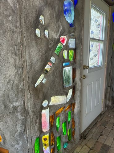 A colorful mosaic art installation embedded in a textured wall near a white door.
