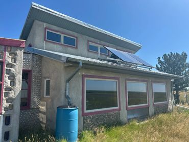 Eco-friendly house with solar panels and rainwater barrel under clear blue sky.