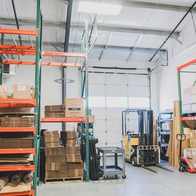 A warehouse with natural light, shelves on the left side, and a forklift on the right side.