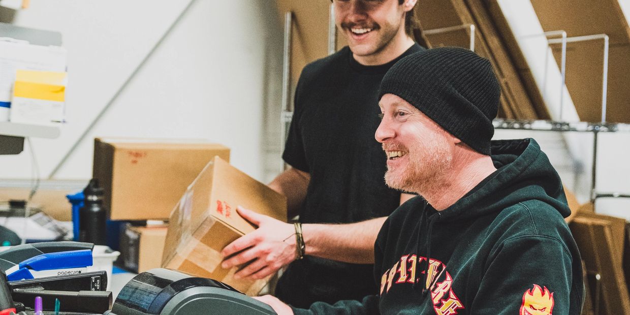 One person is holding a box while the other prints out a shipping label.