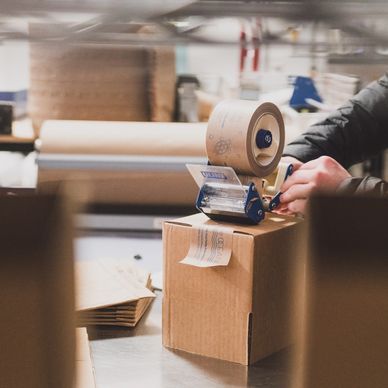 A box is being sealed with paper tape from a tape gun.