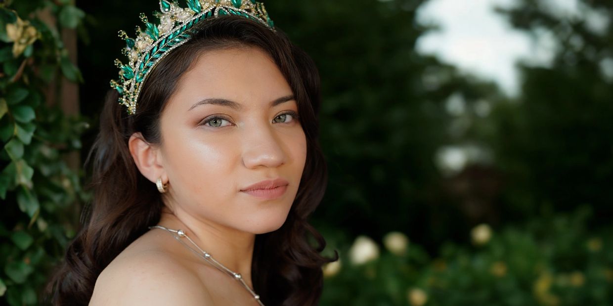 Young woman wearing a green jeweled crown outdoors.