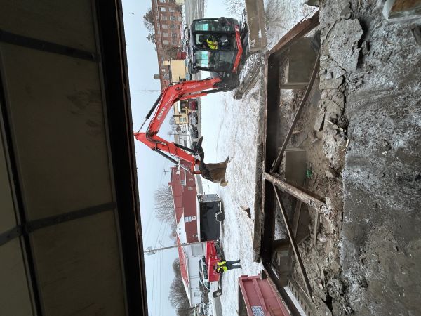 Excavator demolishing a concrete structure in a snowy industrial area.