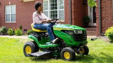 Woman riding a green lawn mower on a sunny day.