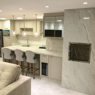Sala gourmet com churrasqueira inox, paredes revestidas em mármore branco Paraná acetinado.