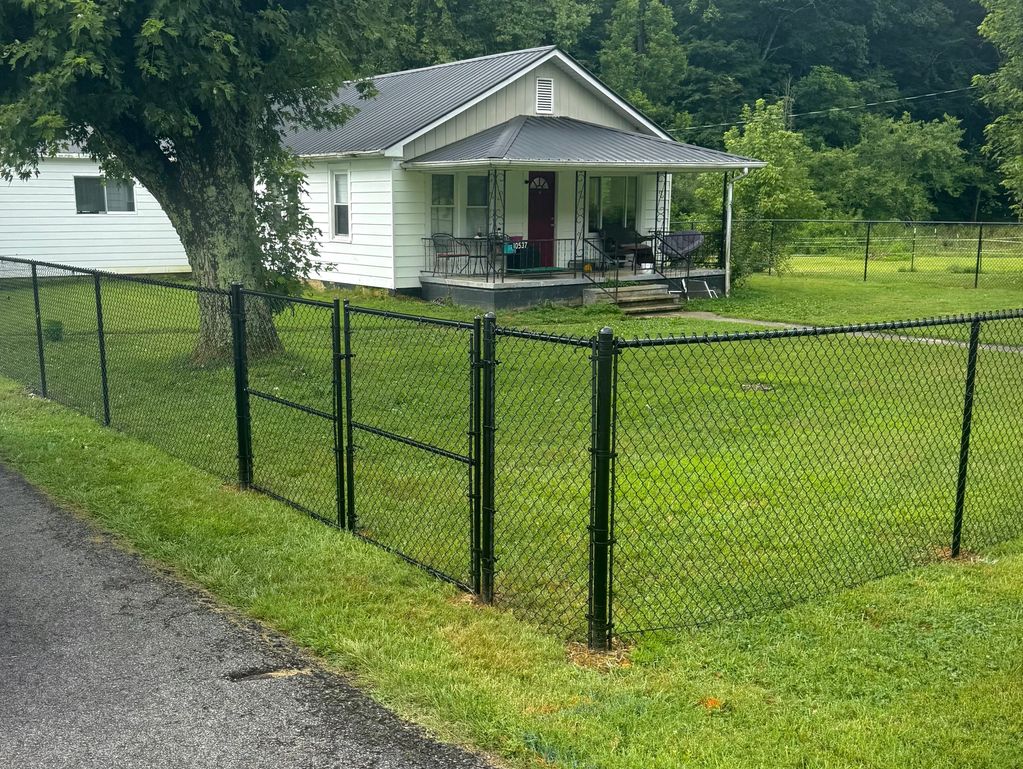 Small white house with a black chain-link fence and green yard. Fencing Services in Kingsport