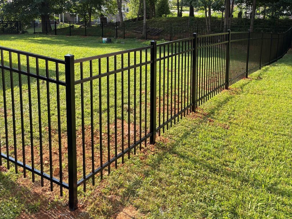 A black metal fence encloses a grassy area with trees. Fencing Services in Kingsport
