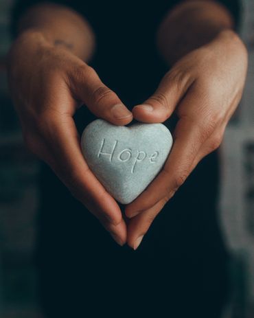 close up picture of hands holding a stone in a love shape