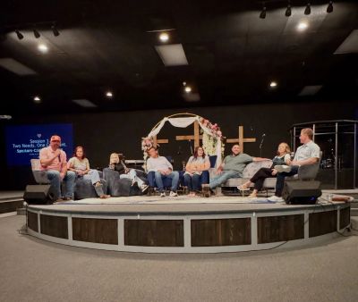Panel discussion on stage with cross and arch in background.