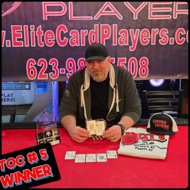 Man holding winning poker hand at a tournament with trophy and merchandise.